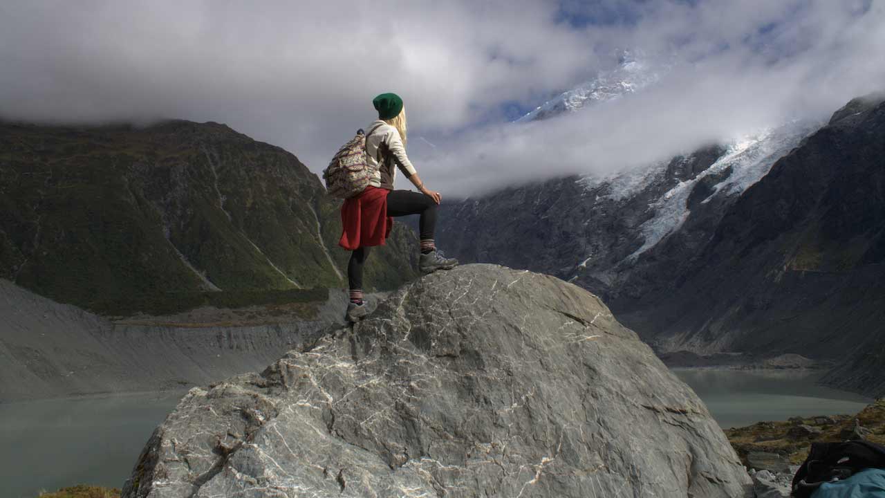 A girl poses on a rock facing cloud covered mountains in New Zealand