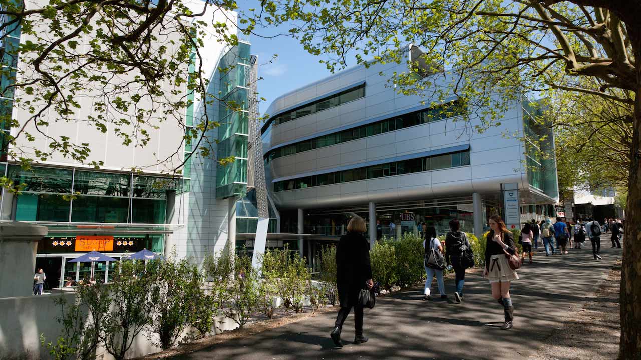 Students walk along a courtyard between two buildings on University of Auckland's campus