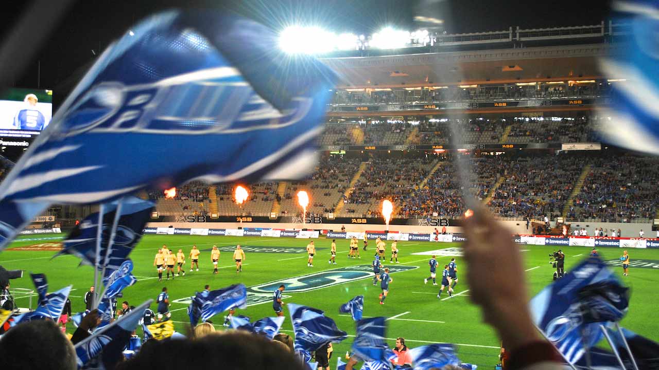 Fans wave flags as they watch a rugby match in Auckland