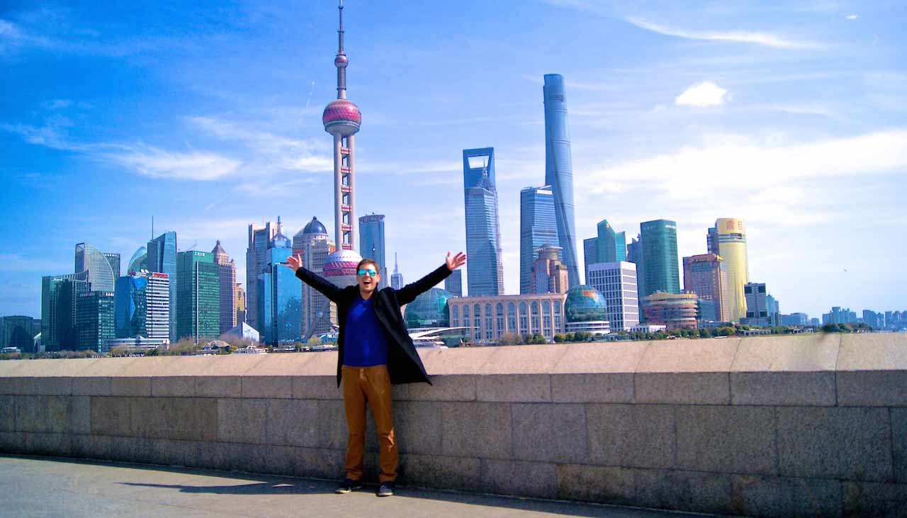 A man has his arms up in excitement while standing in front of the Shanghai cityscape