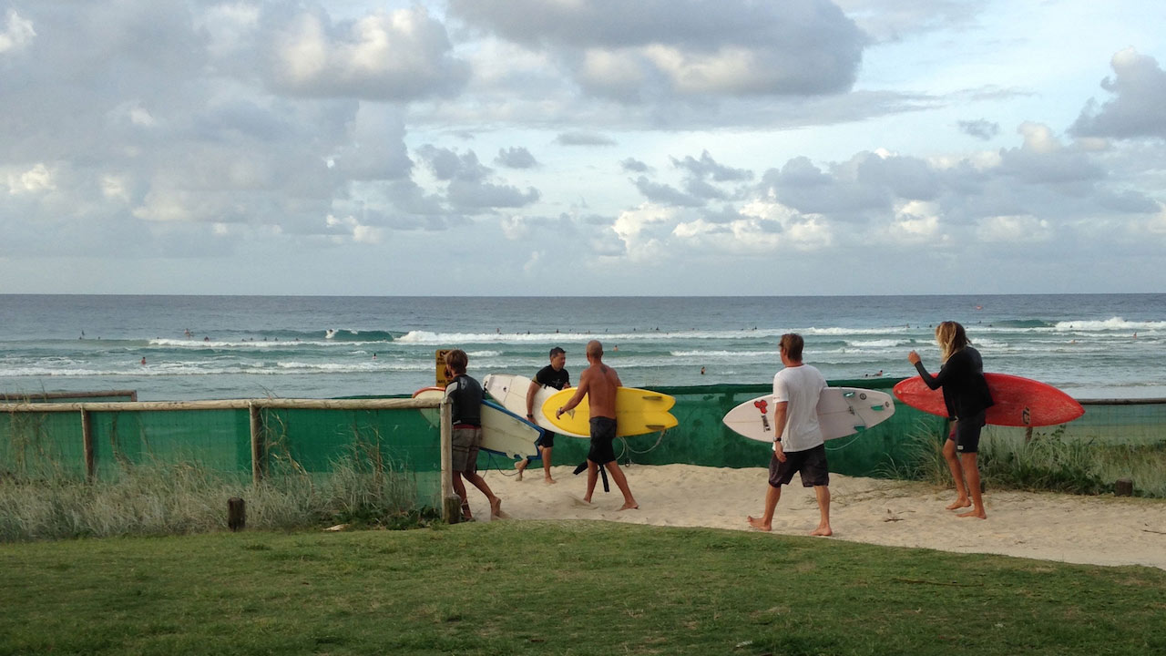 Four people walking with surfboards on a sandy path to the beach on the Gold Coast