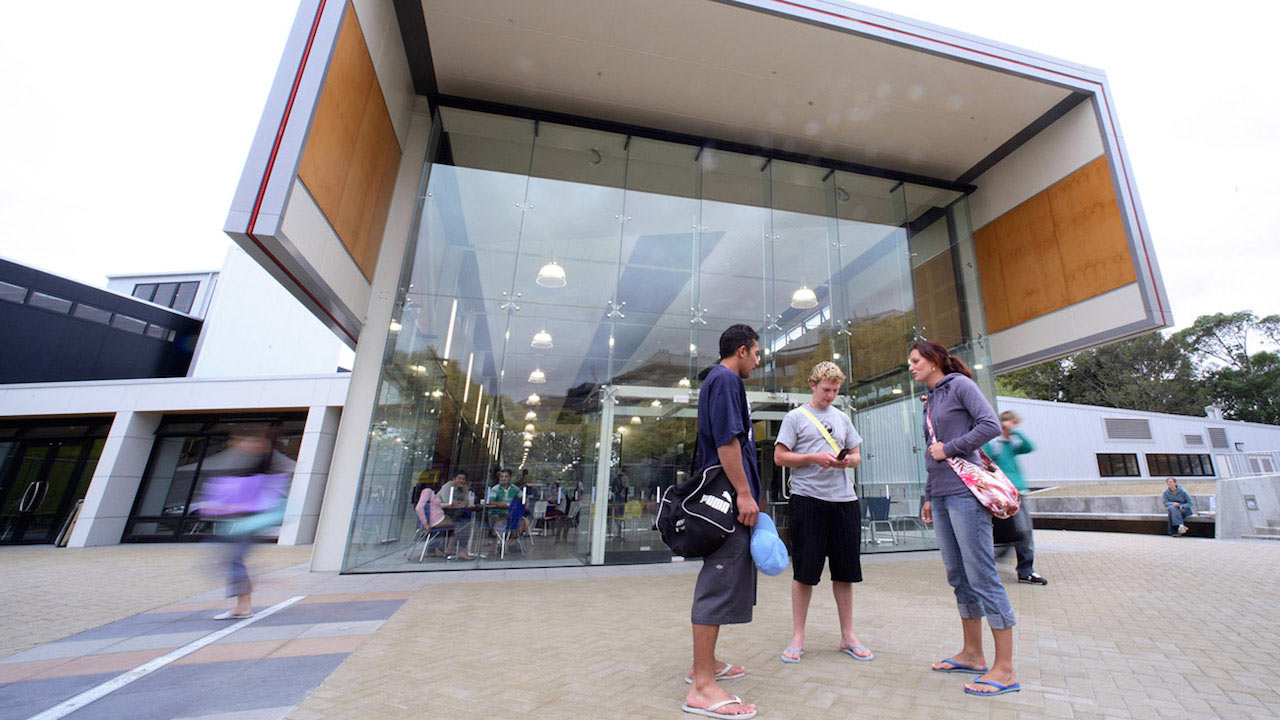 Three people stand outside a modern building on Massey University Palmerston North campus