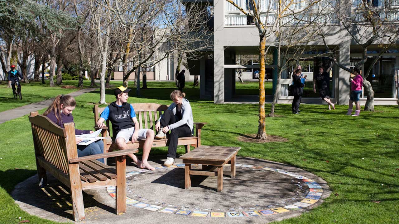 Three people sit on benches conversing outside on Massey University Palmerston North campus