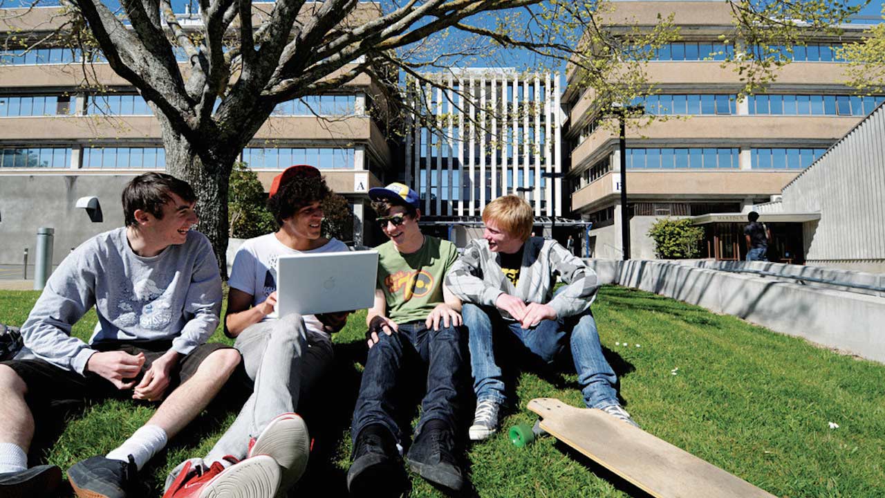 Four boys sit together on the grass talking on Massey University Palmerston North's campus
