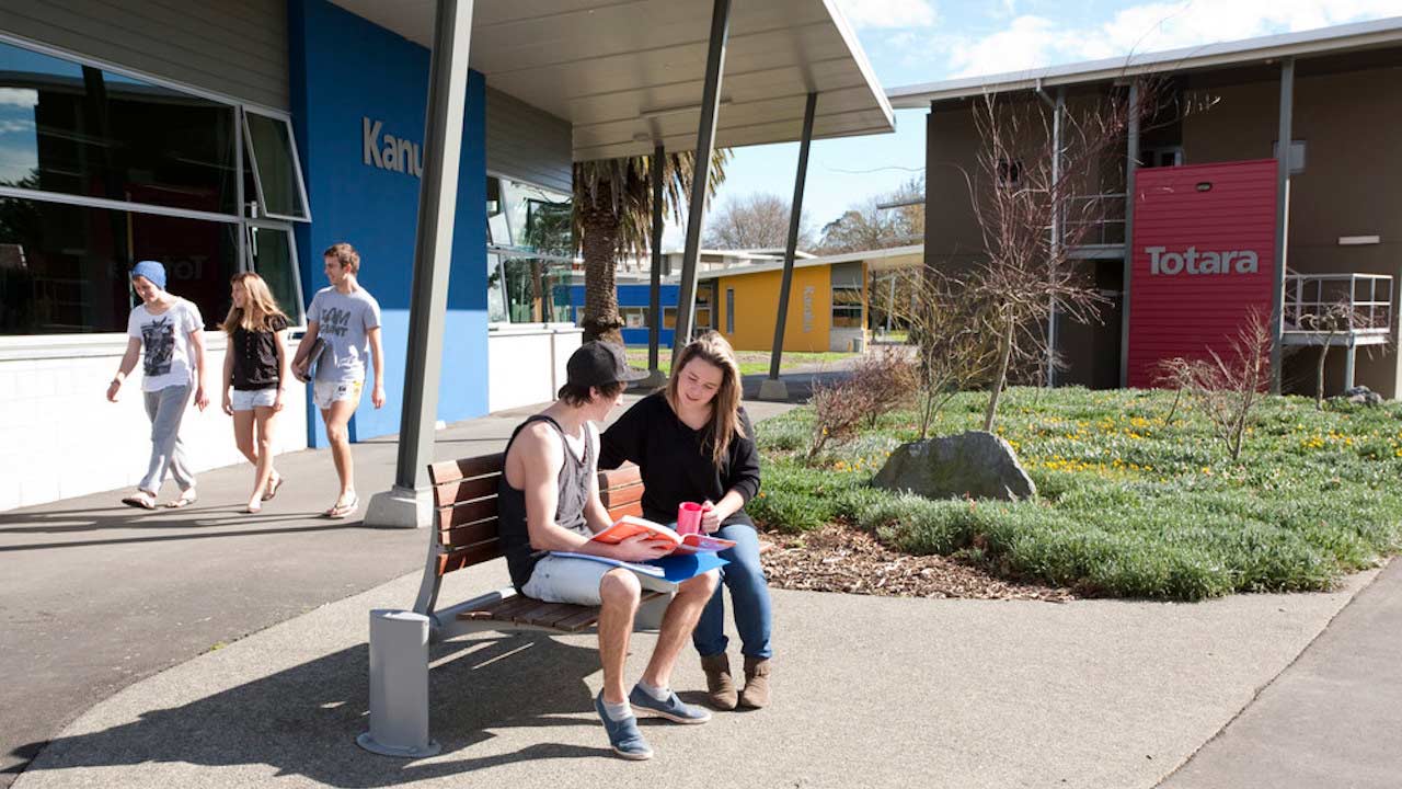 Two people sit conversing on a bench while others walk by on Massey University- Palmerston North campus