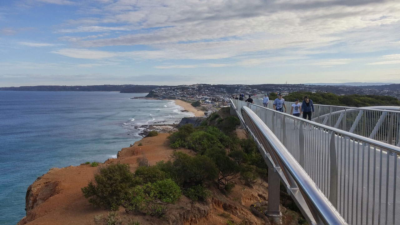 People walk along the foot bridge built alongside the coast in Newcastle, Australia