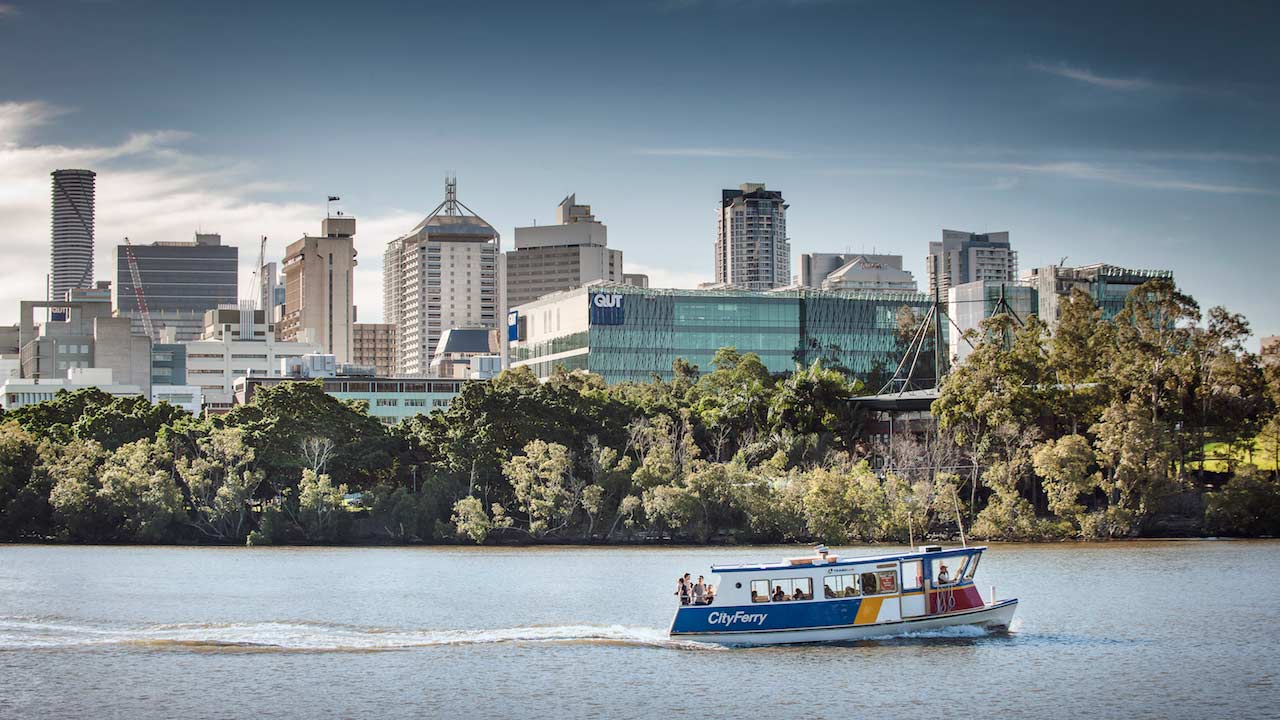A ferry chugs along the Brisbane River past QUT's campus