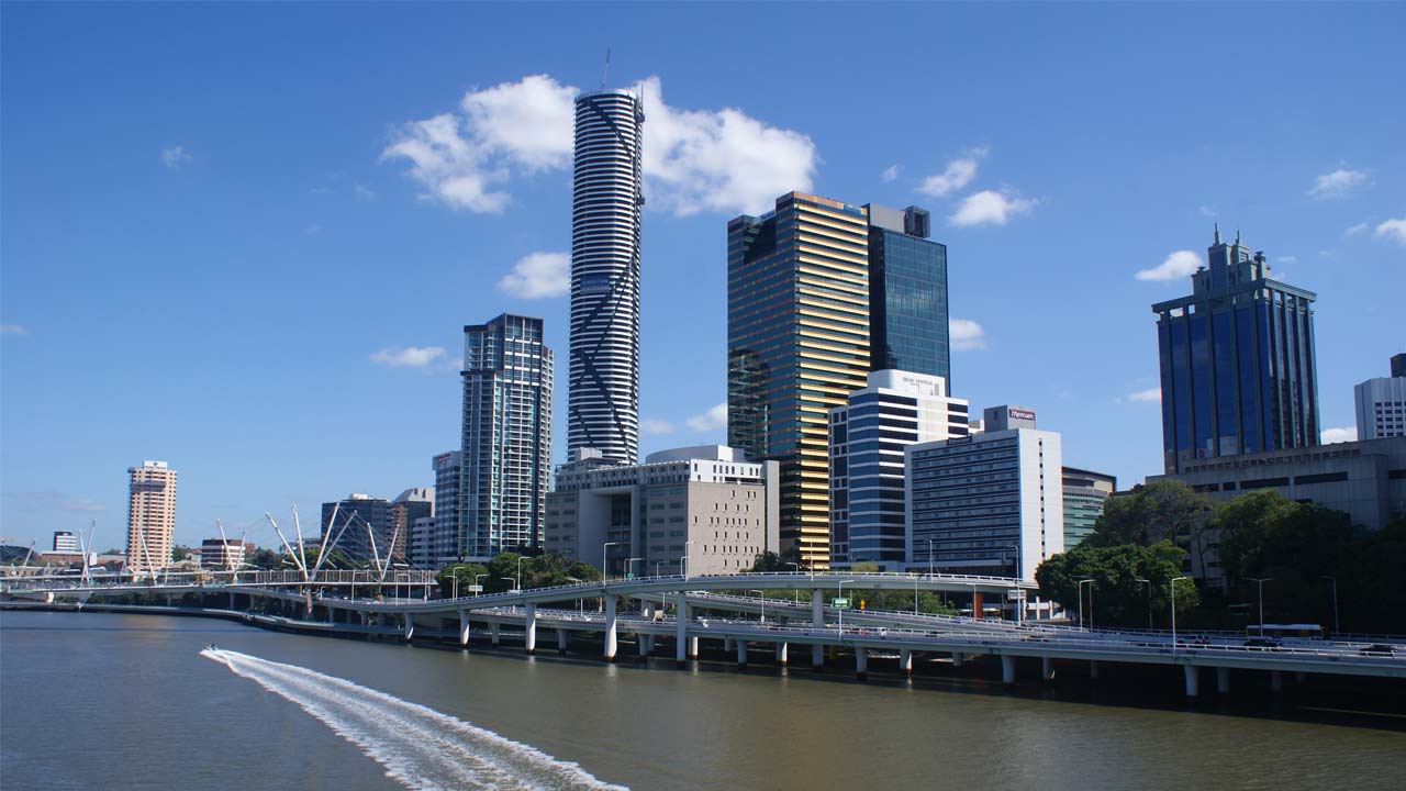 A boat cruises down the Brisbane River beside a business district