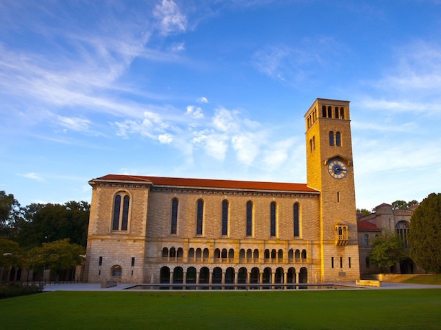 An ornate, brick building erect near a grassy quad below a blue sky on University of Western Australia's campus in Perth