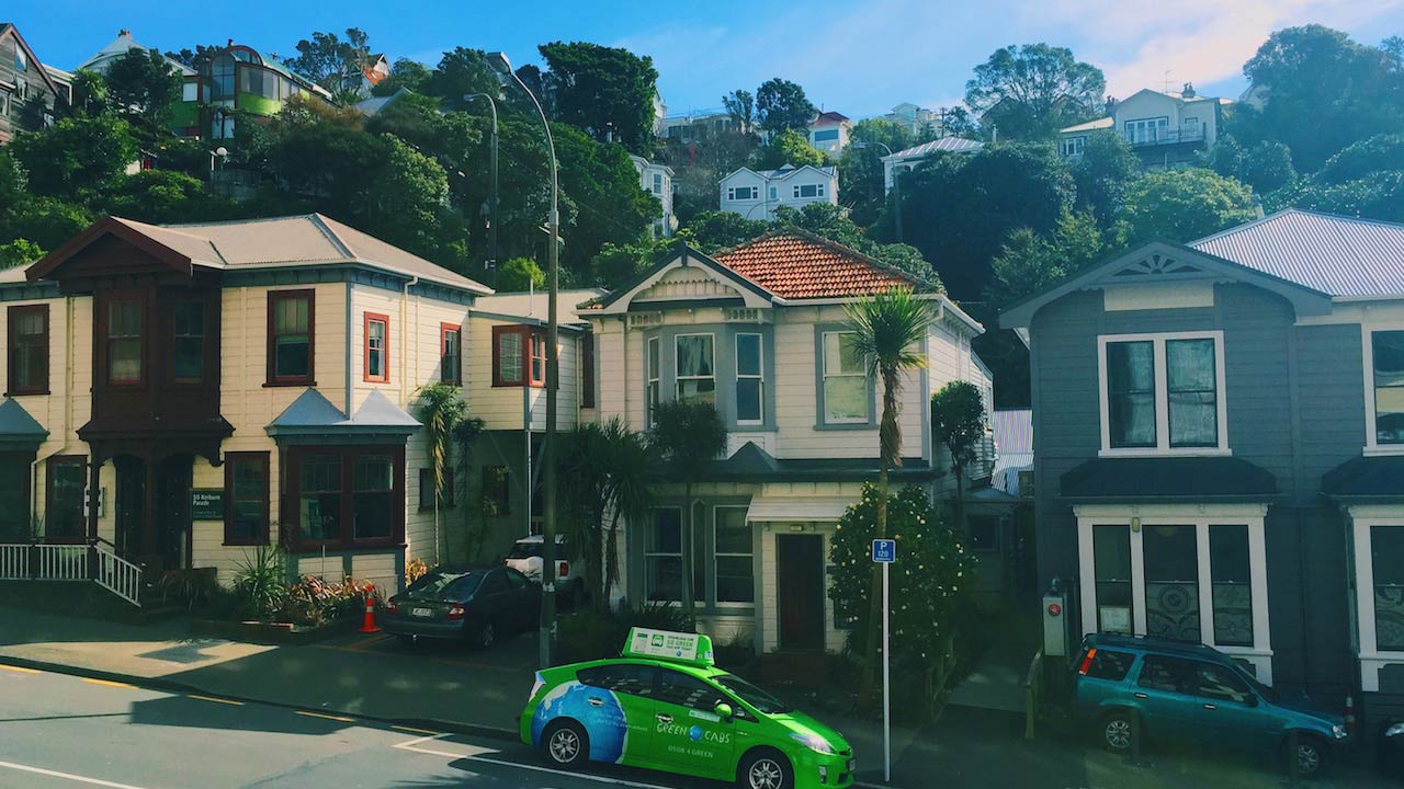 A green car parked in front of a row of houses in Wellington, New Zealand