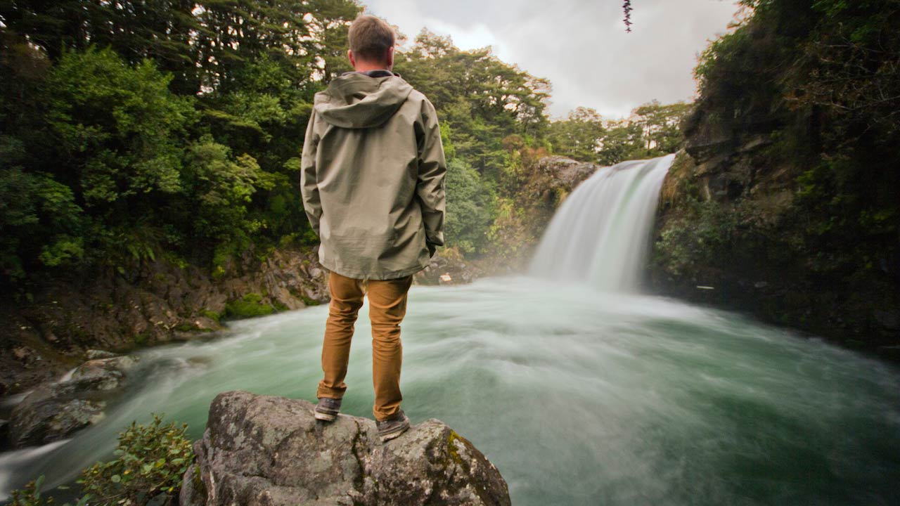 A man stands on a rock looking at a rushing waterfall near Wellington, New Zealand