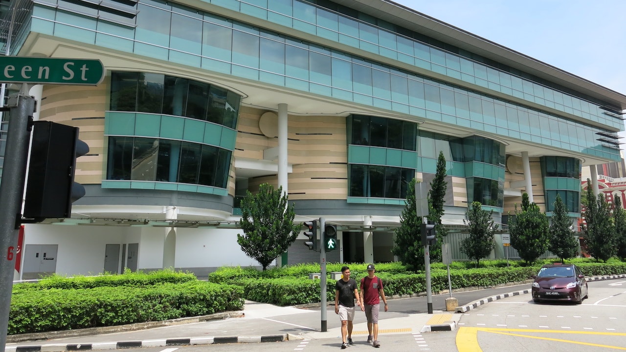 Two people walk on the sidewalk next to a building on Singapore Management University's campus